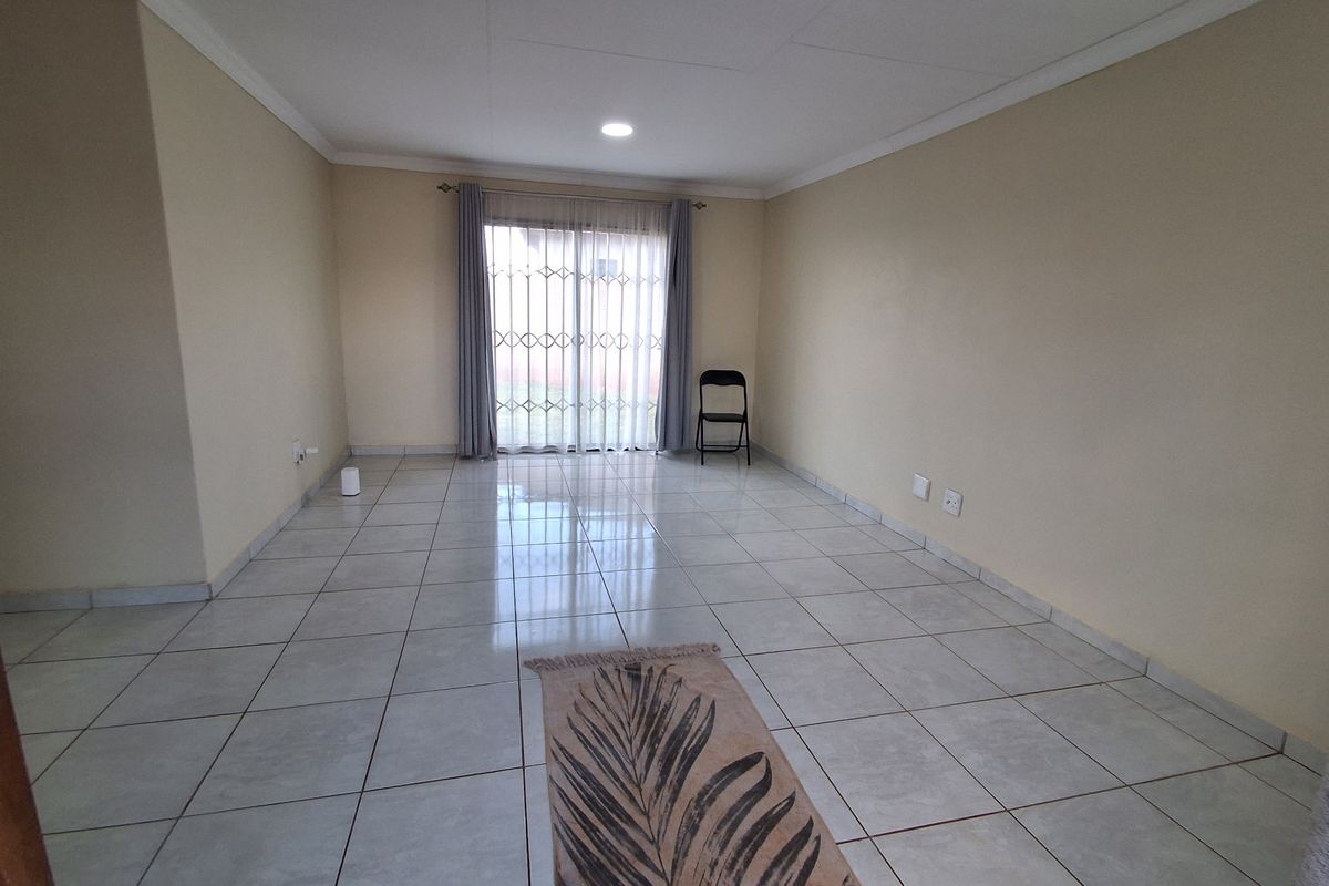 A spacious, empty living room featuring neutral walls, tiled flooring, and a sliding glass door with a security gate leading to the exterior.