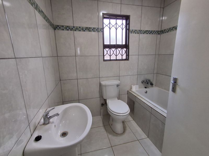 A functional bathroom featuring a pedestal basin, toilet, and built-in bathtub with neutral wall and floor tiling.