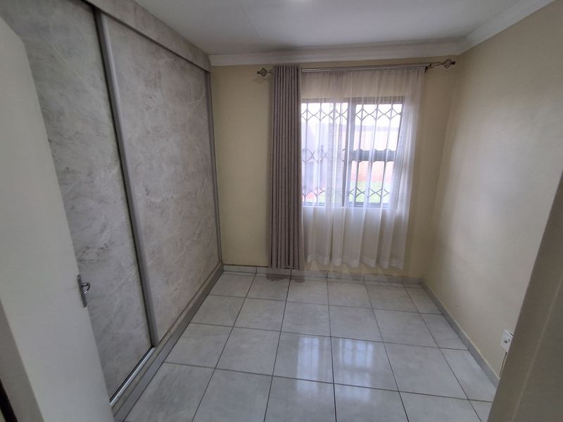 A clean, empty bedroom featuring neutral tiled flooring and a modern built-in sliding door wardrobe with a marble-effect finish.