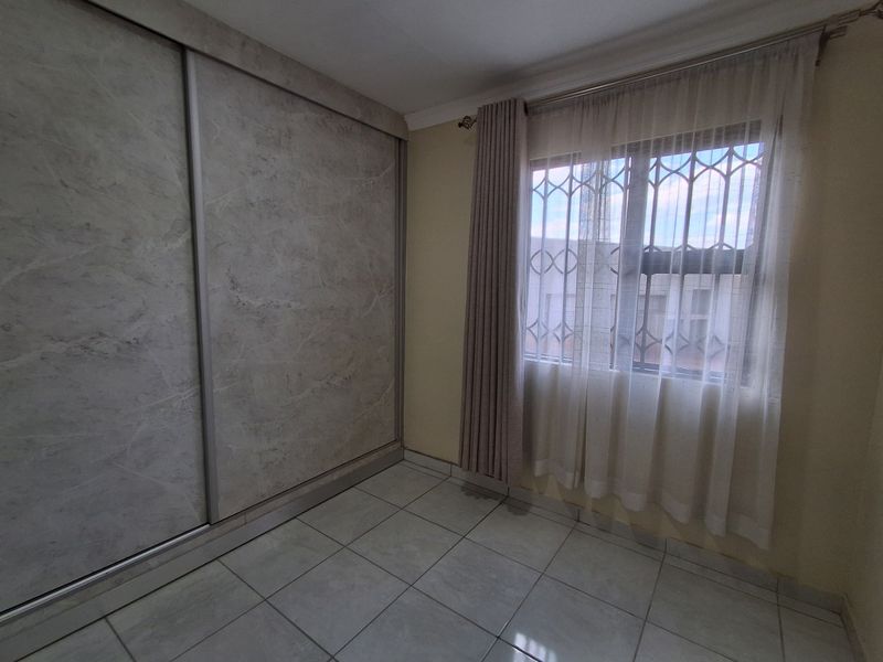 A clean, empty bedroom featuring modern marble-effect sliding door built-in cupboards, tiled flooring, and a window fitted with security bars.