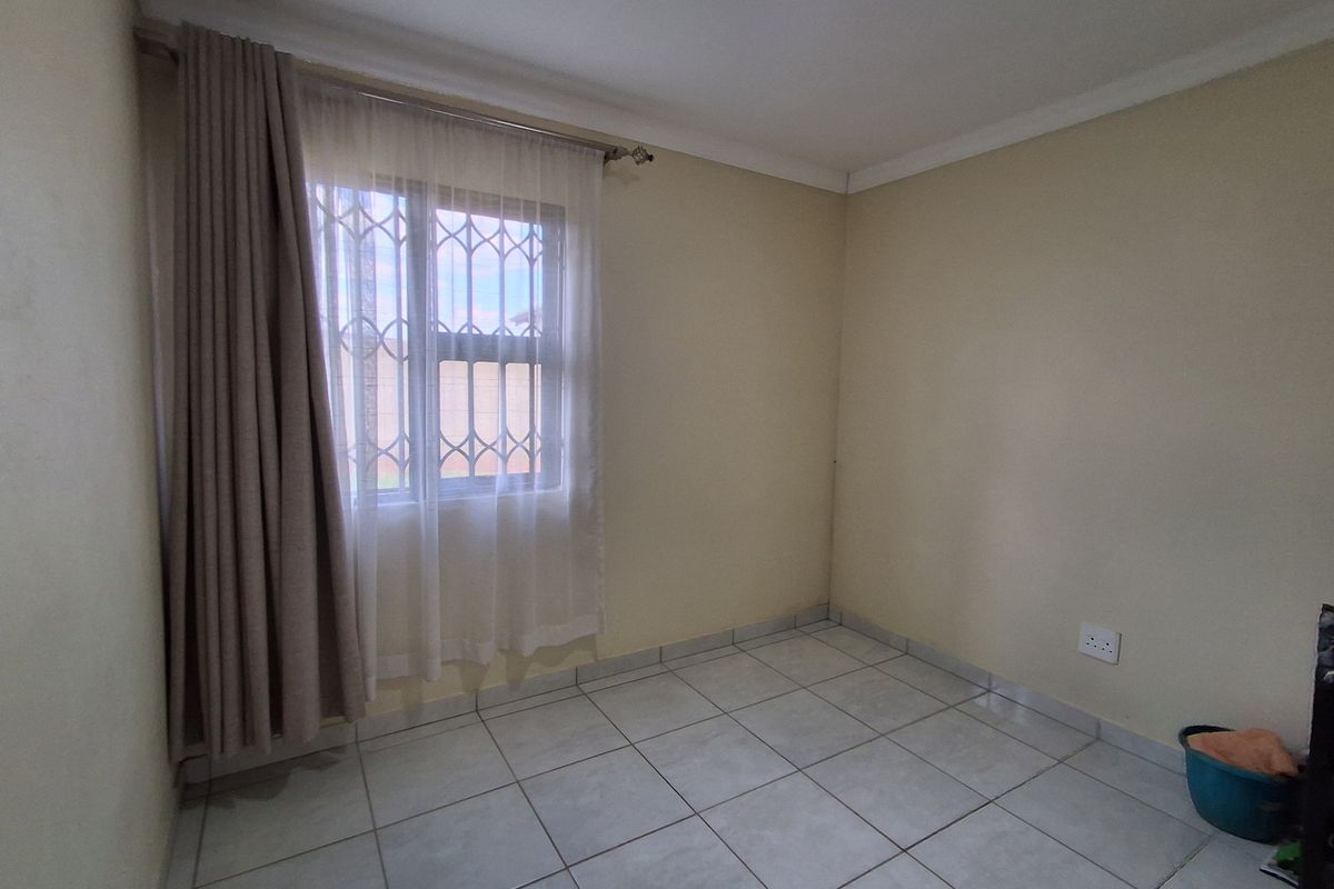 A clean, empty bedroom featuring neutral tiled flooring, security bars on the window, and simple coving detail.