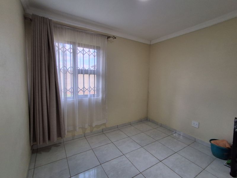 A clean, empty bedroom featuring neutral tiled flooring, security bars on the window, and simple coving detail.