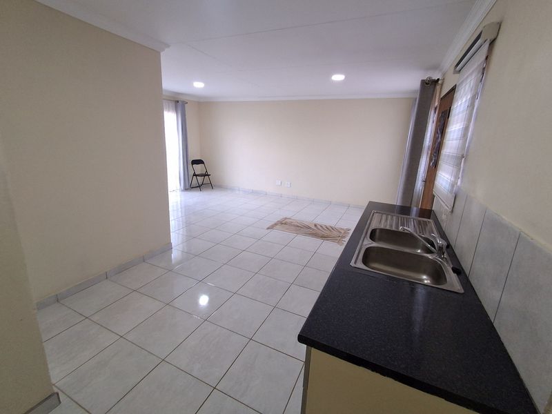 Spacious open-plan living area featuring tiled flooring, recessed lighting, and a functional kitchen section with a double bowl sink and dark laminate countertops.