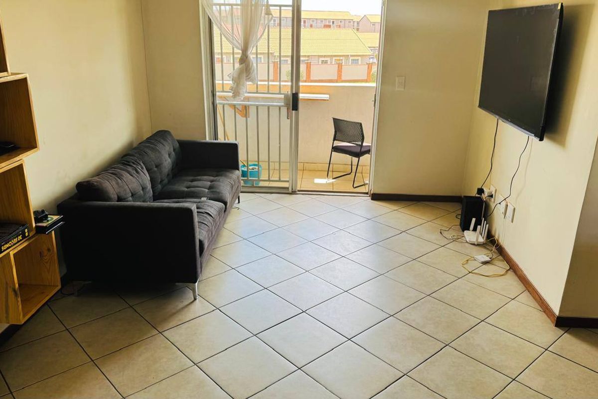 A living room featuring tiled flooring and a sliding glass door leading to a balcony, providing natural light and access to outdoor space.