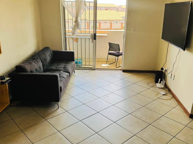 A living room featuring tiled flooring and a sliding glass door leading to a balcony, providing natural light and access to outdoor space.
