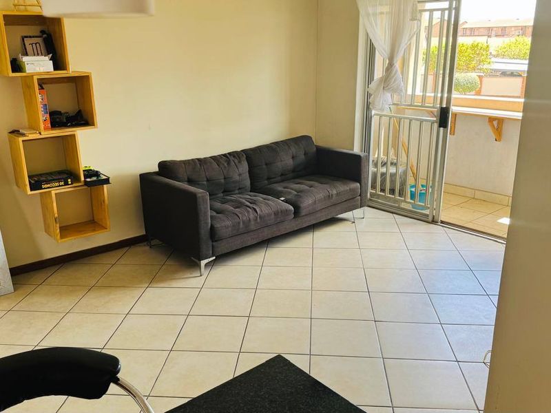 A living room featuring tiled flooring and a sliding glass door with a security gate, providing access to an outdoor balcony area.