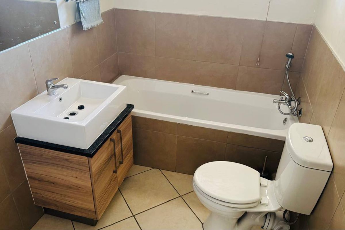 A functional bathroom featuring a modern vanity with basin, a standard bathtub with handheld shower mixer, and neutral wall and floor tiling.