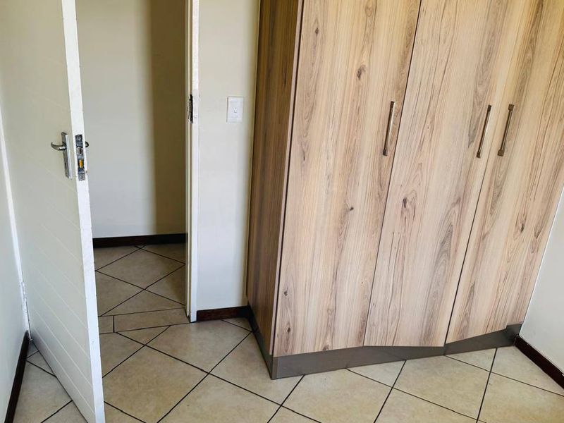 A clean bedroom featuring light wood-finish built-in wardrobes, neutral walls, and tiled flooring with a doorway leading to an adjacent space.