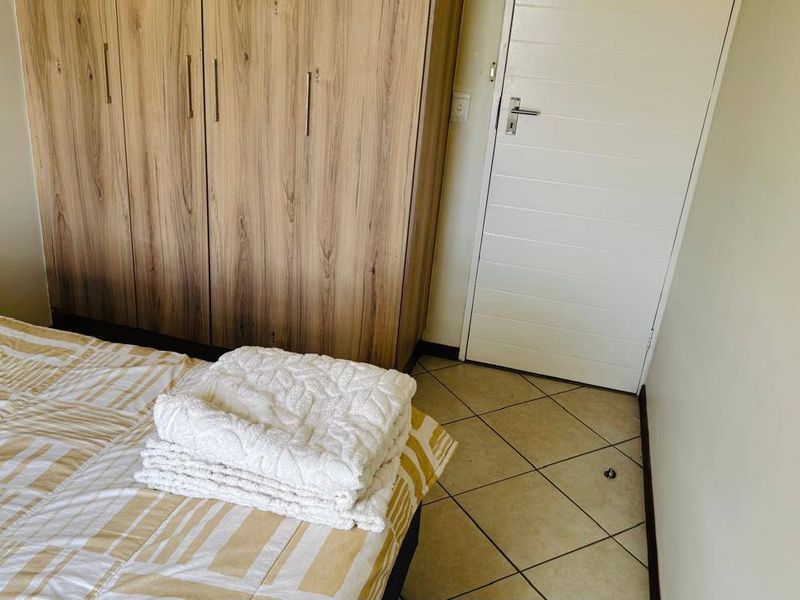 A bedroom featuring built-in wooden cupboards, tiled flooring, and a white internal door.