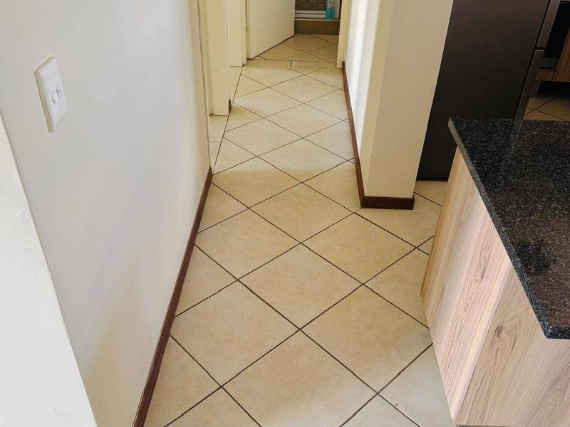 A view of a tiled hallway leading towards other rooms, featuring adjacent kitchen cabinetry with a granite countertop.