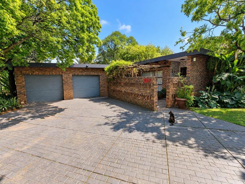 Front elevation of a brick house featuring a double garage, paved driveway, and a charming brick boundary wall with a pergola entrance.