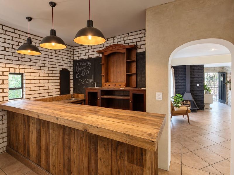 A rustic-style bar area featuring a built-in wooden counter, sink, and exposed brick walls, leading through an archway into an adjacent living space.