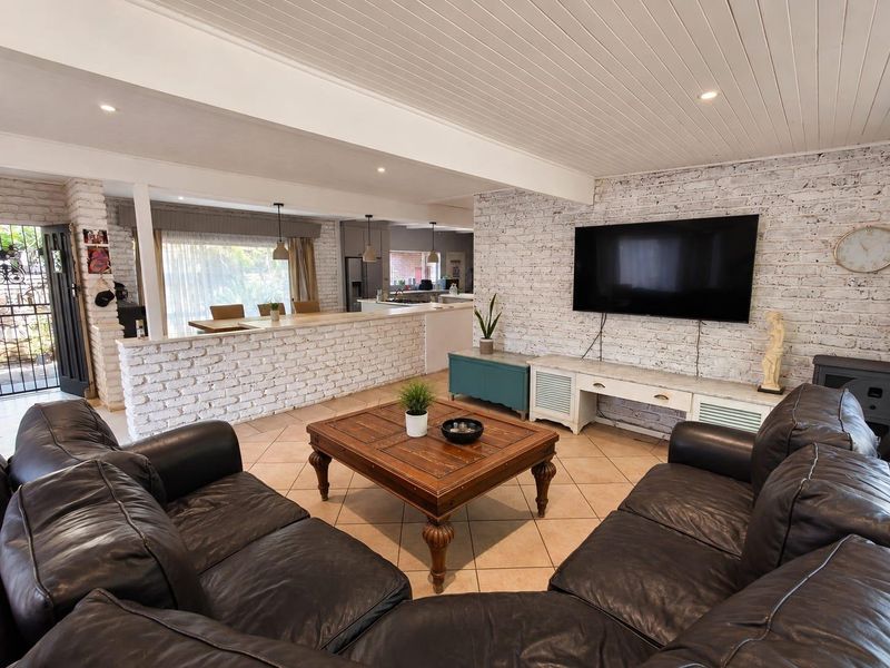 Spacious open-plan living area featuring a white-washed exposed brick wall, tiled flooring, and a timber ceiling, seamlessly connecting to the kitchen and breakfast bar.