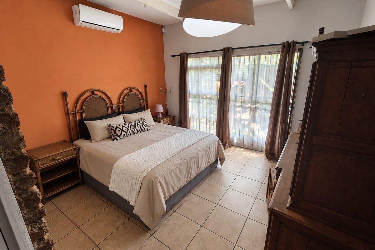 A bedroom featuring tiled flooring, exposed ceiling beams, a wall-mounted air conditioner, and sliding glass doors providing natural light.