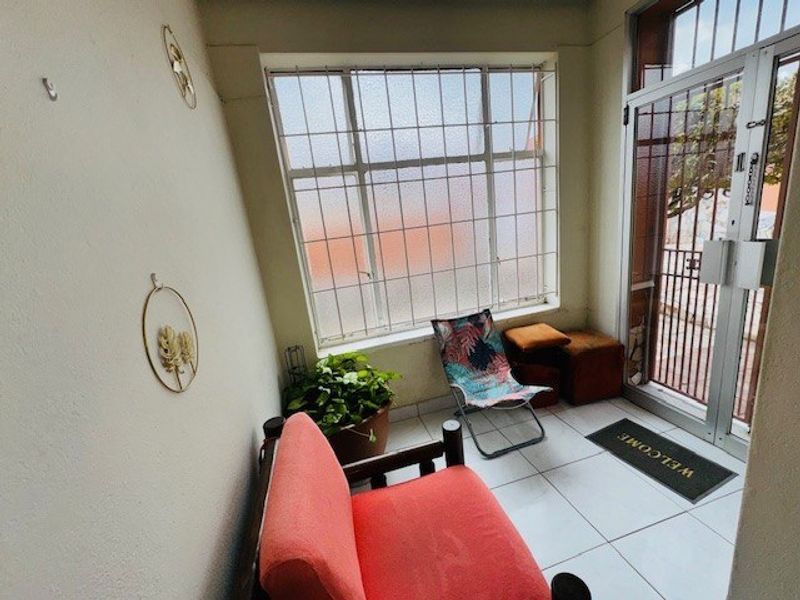 A bright entrance area featuring tiled flooring, a large window with security bars, and a secure metal entrance gate.