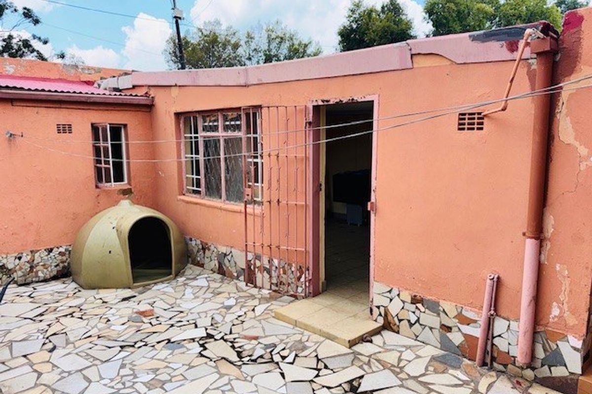 Rear exterior view of the property featuring a paved courtyard, security gate, and weathered wall finishes requiring maintenance.