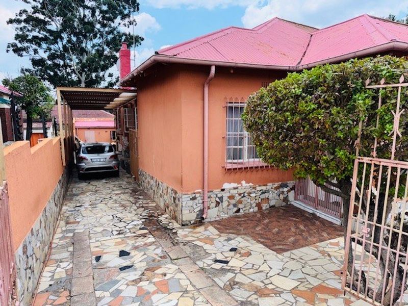 Exterior view of a house featuring a metal roof, stone cladding accents, a paved driveway with a carport, and secure boundary fencing.