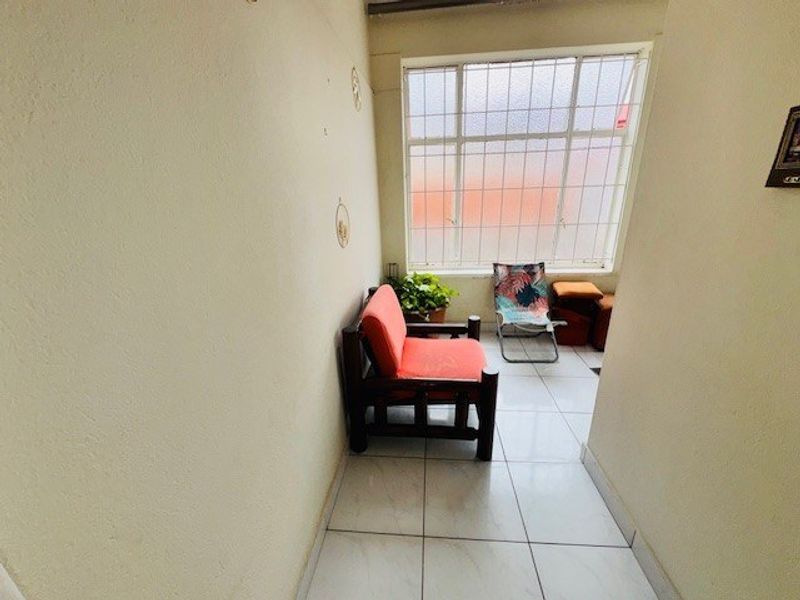 A small, enclosed sunroom or patio area featuring tiled flooring and a large window with security bars, offering a bright, functional space.
