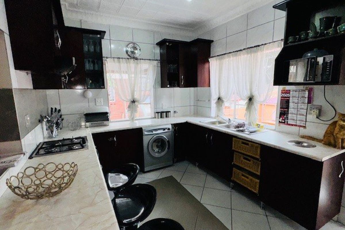 A functional kitchen featuring dark wood cabinetry, light laminate countertops, a gas hob, and an integrated washing machine with tiled finishes throughout.