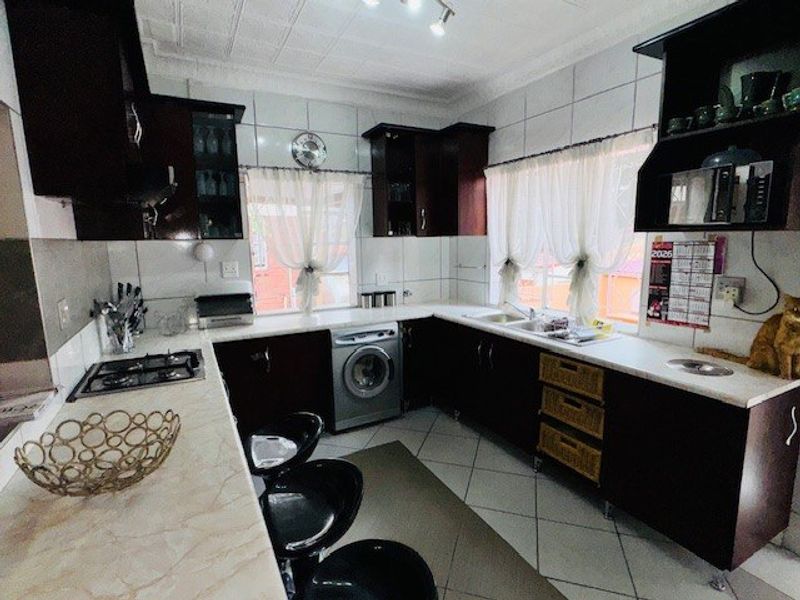 A functional kitchen featuring dark wood cabinetry, light laminate countertops, a gas hob, and an integrated washing machine with tiled finishes throughout.