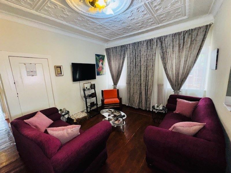 A living room featuring original pressed metal ceilings, a decorative ceiling rose, and polished hardwood flooring.