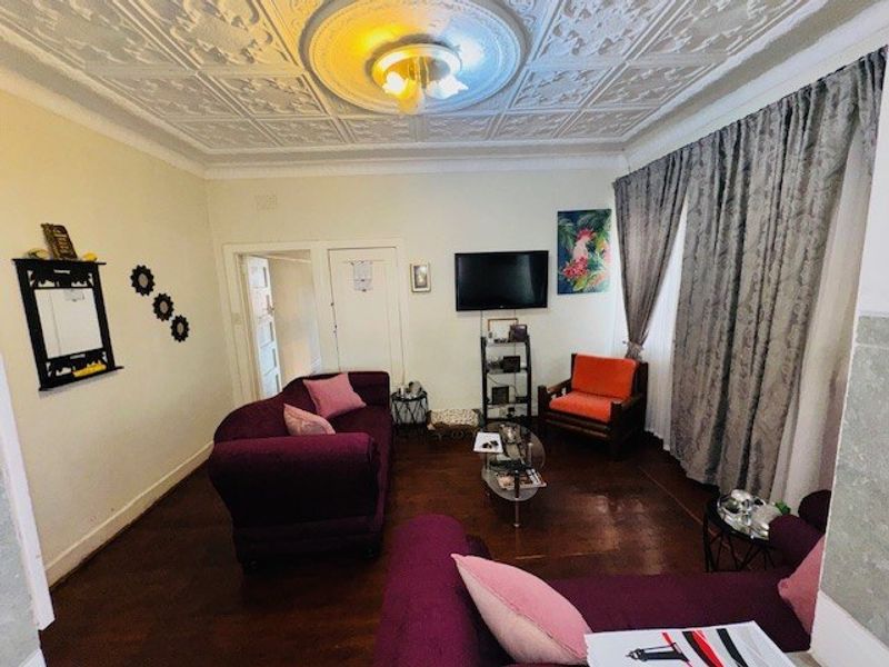 A living room featuring original hardwood flooring and a decorative pressed metal ceiling with a central ceiling rose.