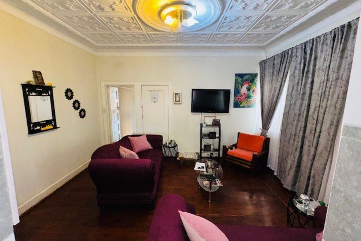 A living room featuring original ornate pressed metal ceilings, a decorative ceiling rose, and polished hardwood flooring.