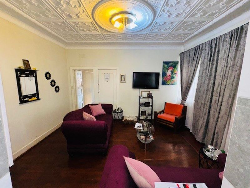 A living room featuring original ornate pressed metal ceilings, a decorative ceiling rose, and polished hardwood flooring.