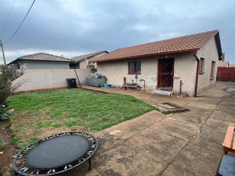 Rear view of the property featuring a paved patio area, small lawn, and perimeter walling with visible exterior maintenance required.