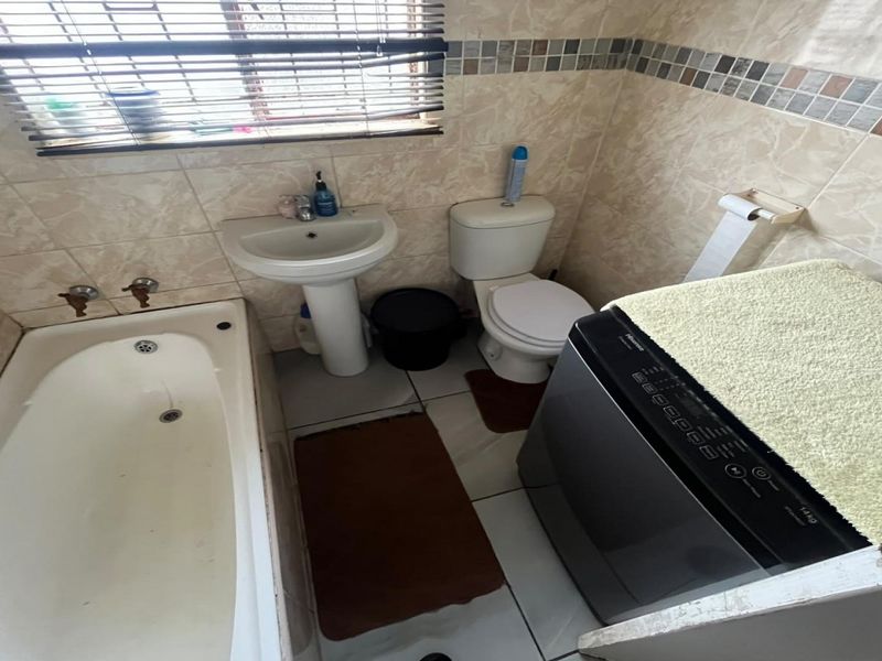 Compact bathroom featuring a pedestal basin, toilet, and bathtub with neutral wall tiling and floor tiles.