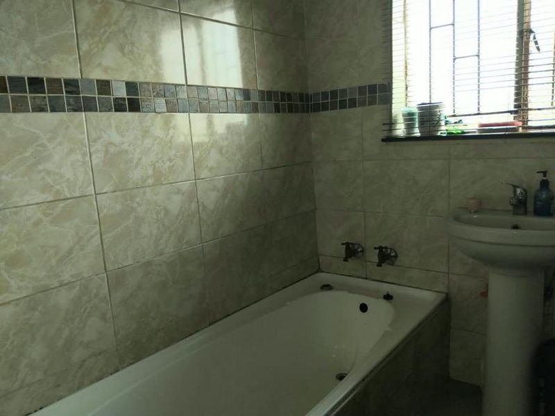 A functional bathroom featuring a built-in bathtub, pedestal basin, and tiled walls with a decorative mosaic border.