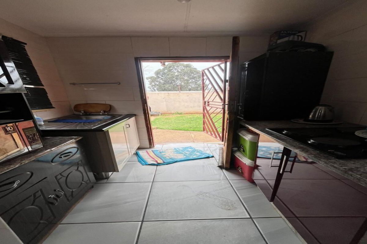 A compact kitchen featuring built-in cabinetry, tiled flooring, and direct access to the rear garden through a security gate.