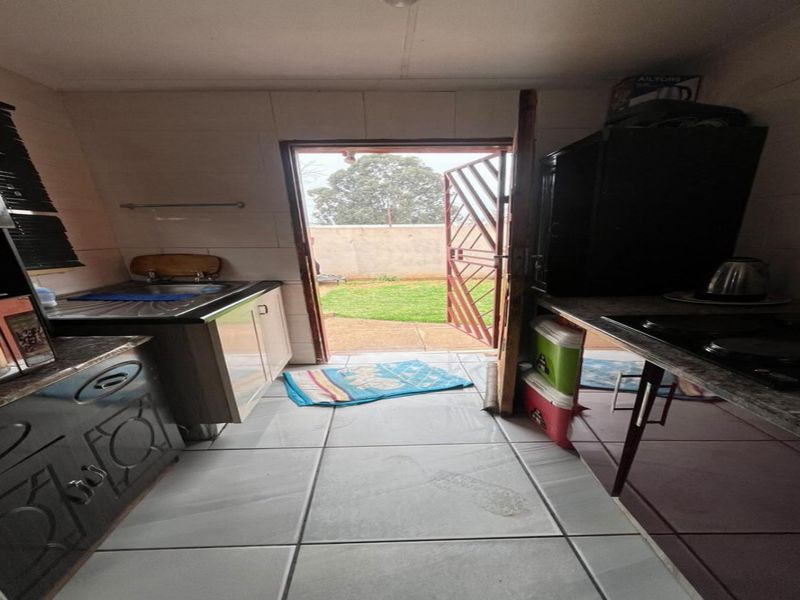 A compact kitchen featuring built-in cabinetry, tiled flooring, and direct access to the rear garden through a security gate.
