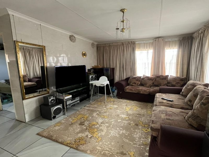 A living room featuring tiled flooring and tiled wall finishes, offering a functional space with natural light through large window curtains.