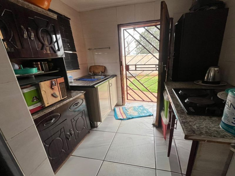 Compact kitchen featuring built-in cabinetry, tiled surfaces, and direct access to the rear garden through a security gate.