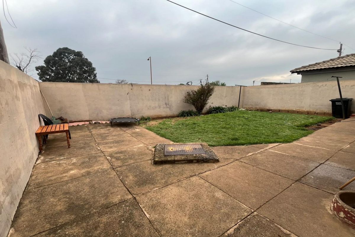 A rear garden area featuring a paved patio space, a small lawn, and a high perimeter boundary wall.