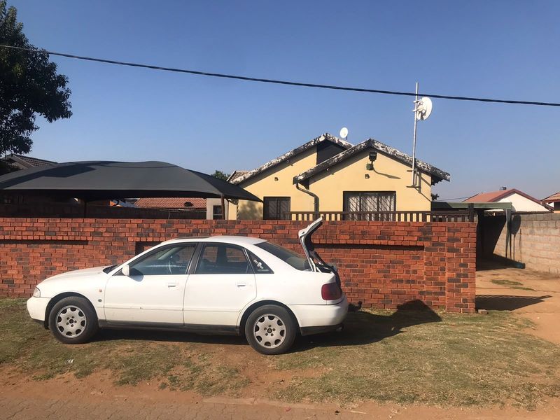 Front exterior view of the property featuring a brick boundary wall, shade cloth carport, and residential dwelling with satellite dish installation.