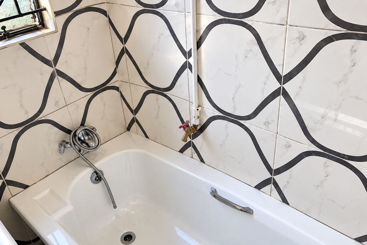 Bathroom featuring a white bathtub with patterned wall tiles, a handheld shower mixer, and a grab rail.