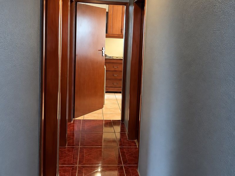 A narrow hallway featuring dark tiled flooring, ornate ceiling cornicing, and wooden door frames leading to adjacent rooms.