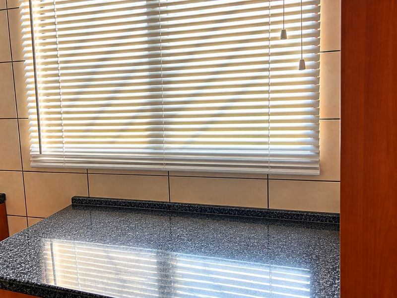 A clean kitchen workspace featuring dark speckled laminate countertops, light ceramic wall tiling, and warm-toned wood veneer cabinetry.