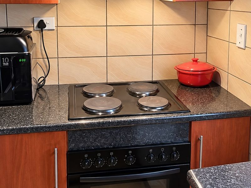 A functional kitchen area featuring built-in cabinetry, a granite countertop, and a fitted electric oven and hob with an overhead extractor fan.