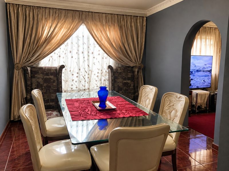 A formal dining room featuring tiled flooring, decorative crown molding, and an arched entryway leading to an adjacent living space.