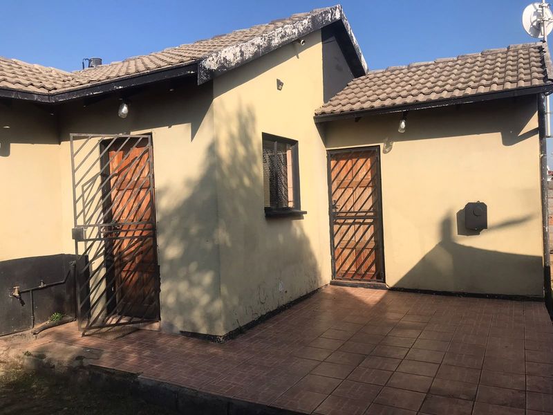 Rear exterior view of the property featuring a tiled patio area, security gates, and wooden doors with visible wear to the roof fascia and walls.