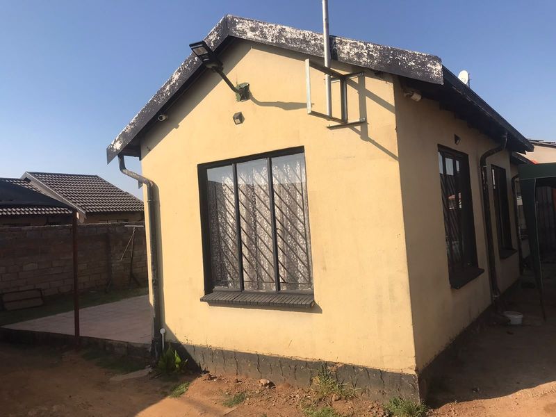 Rear view of the property showing the exterior wall, security bars on windows, and roof fascia requiring maintenance.