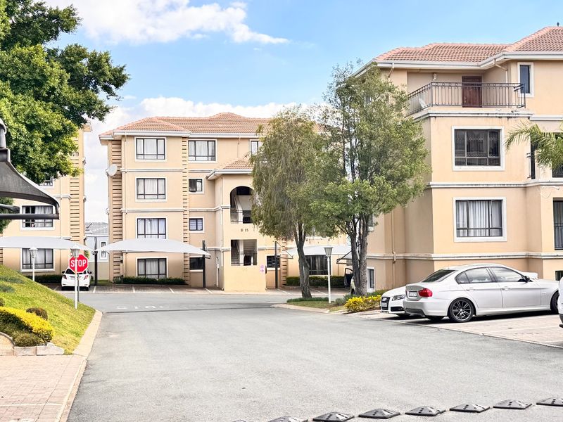 Exterior view of a multi-story apartment complex featuring tiled roofs, balconies, and paved parking areas with shade cloth carports.