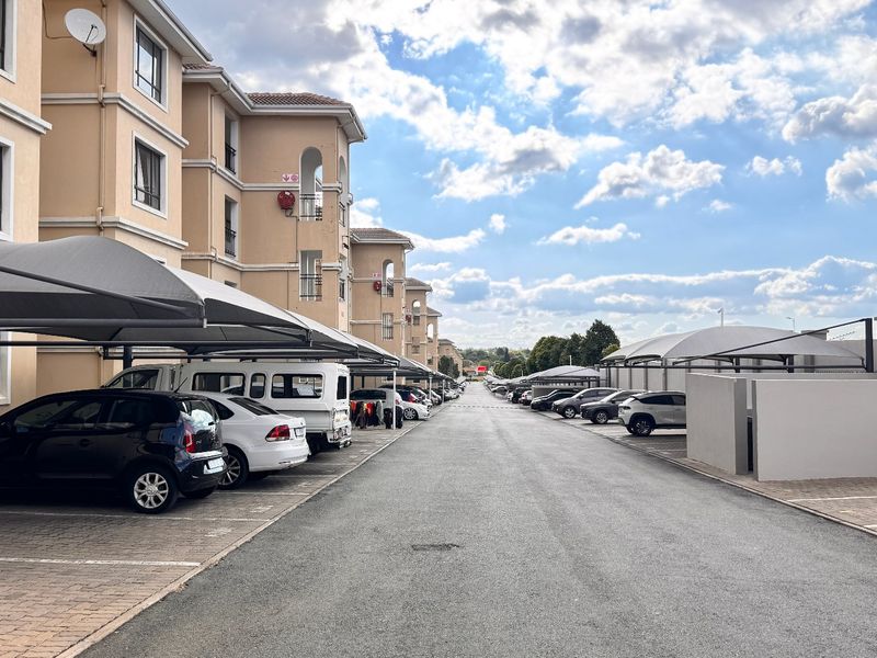Exterior view of an apartment complex featuring a paved driveway, covered parking bays, and multi-story residential building facades.