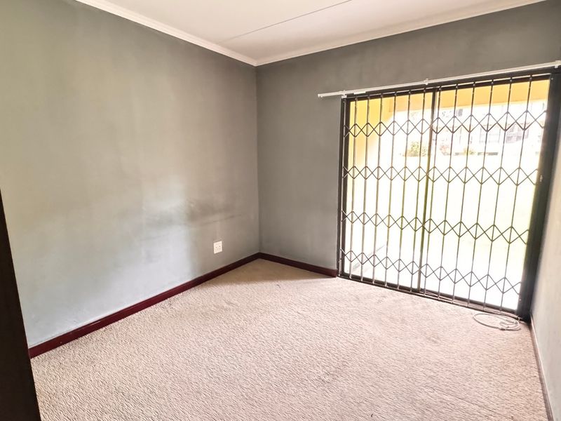 An empty bedroom featuring carpeted flooring and a sliding glass door with a security gate, providing access to the exterior.