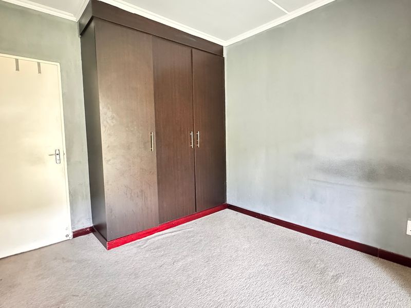 A vacant bedroom featuring a built-in wardrobe, carpeted flooring, and neutral wall finishes, offering a blank canvas for potential updates and personalization.