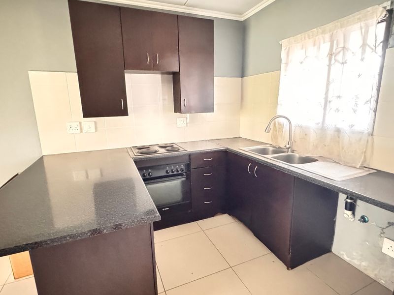A functional kitchen featuring dark wood cabinetry, granite countertops, a built-in oven, and a double sink with tiled backsplash and flooring.