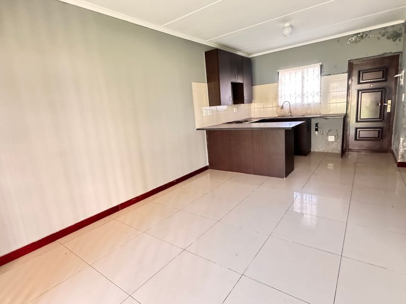 Open-plan living and kitchen area featuring tiled flooring and built-in cabinetry, currently vacant and requiring cosmetic wall repairs.